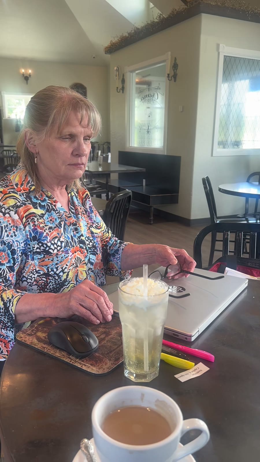 Carla at a table with her laptop, coffee, and notebooks
